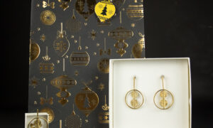 Coffret de Noël Jojo Création Ornement Akan avec parure de bijoux dorés devant un sac cadeau noir décoré de boules de sapin dorées